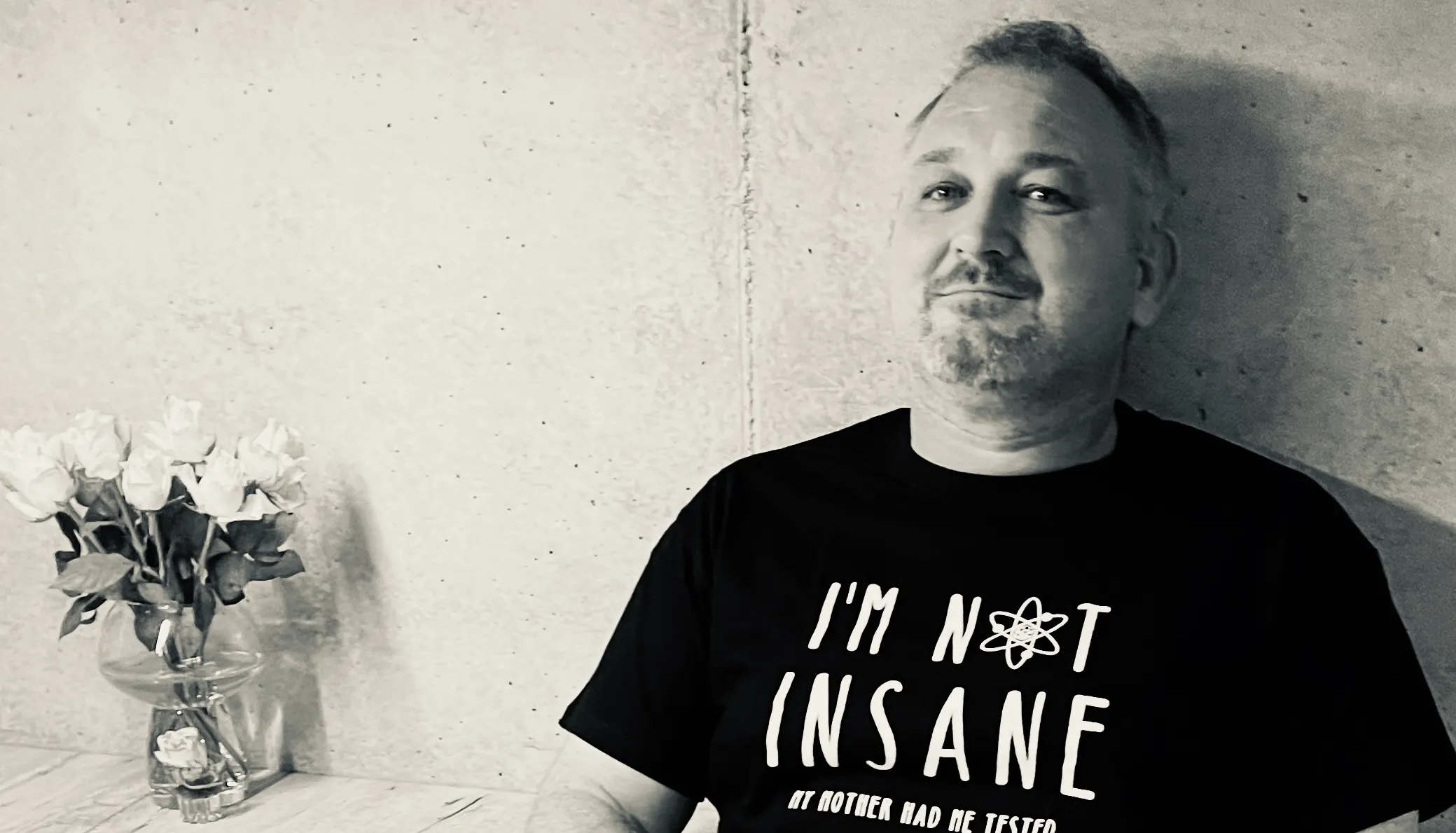 Schwarz-Weiß-Foto: Mann im T-Shirt mit der Aufschrift „I’m not insane“ vor einer Betonwand