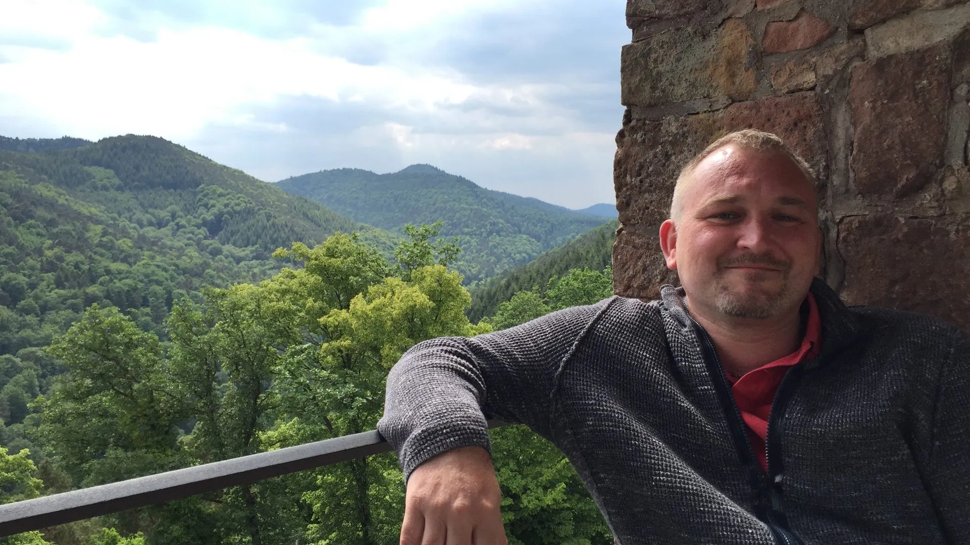 Karsten Zimmer lehnt an einer Burgmauer aus Sandstein, im Hintergrund bewaldete Hügel